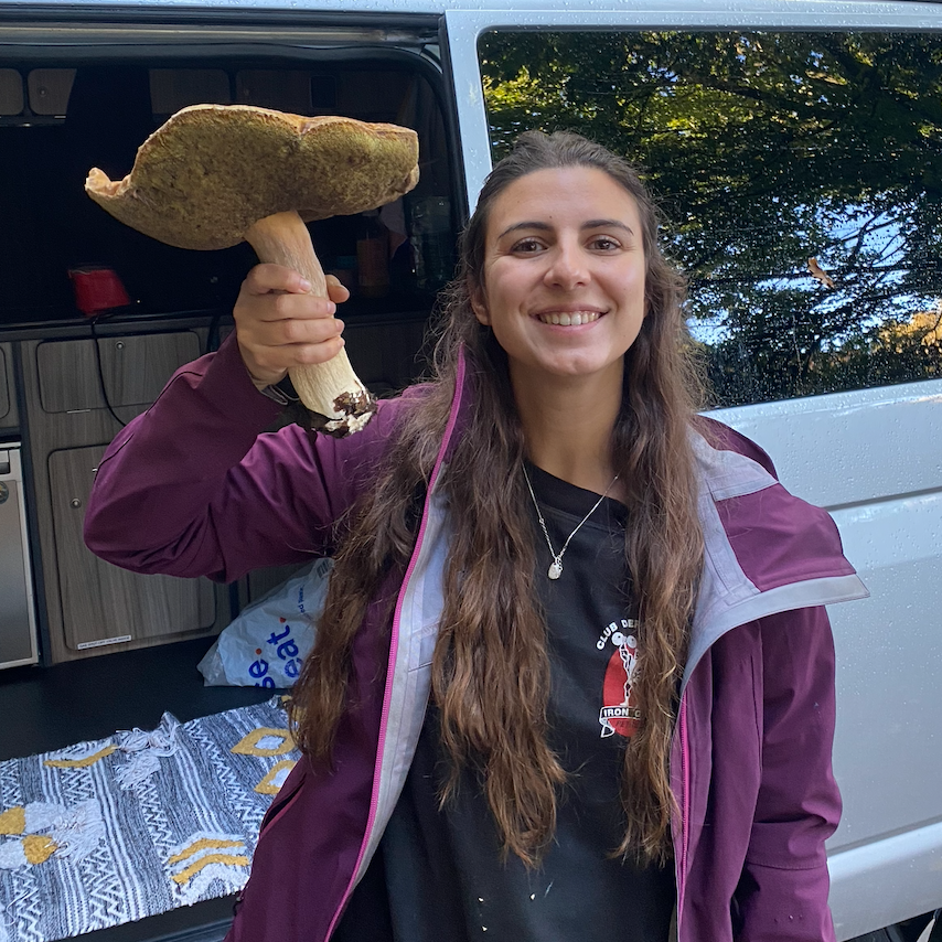 Celia Alonso, the author of the page, holding a big bay bolete mushroom in front of a van